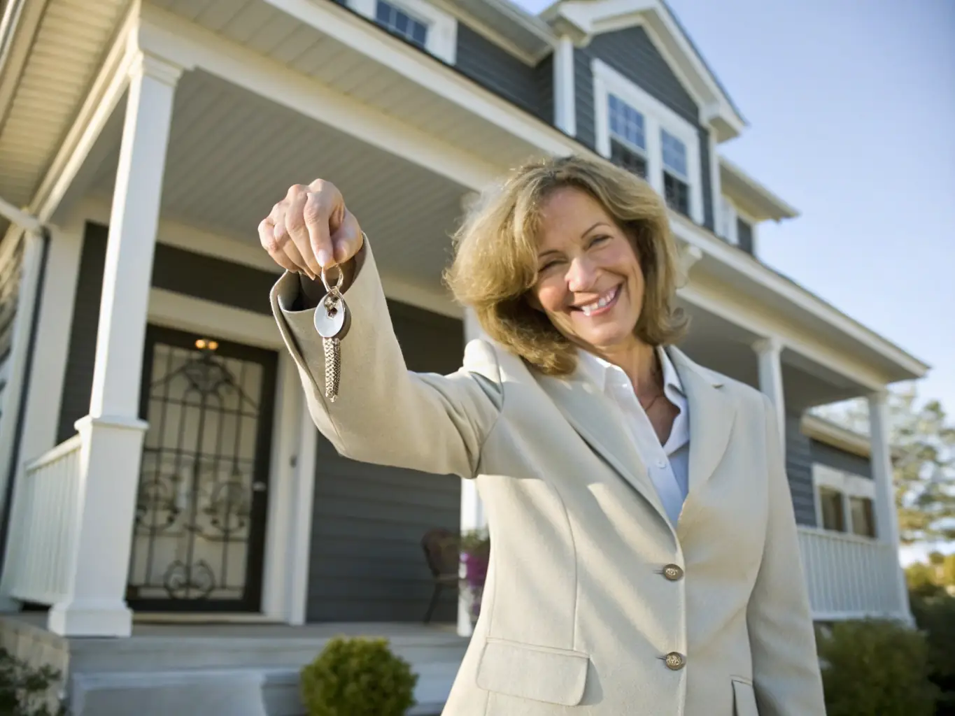 A person smiling while holding keys to a new car, parked in front of their house, representing car loan options from Lenders Depot.